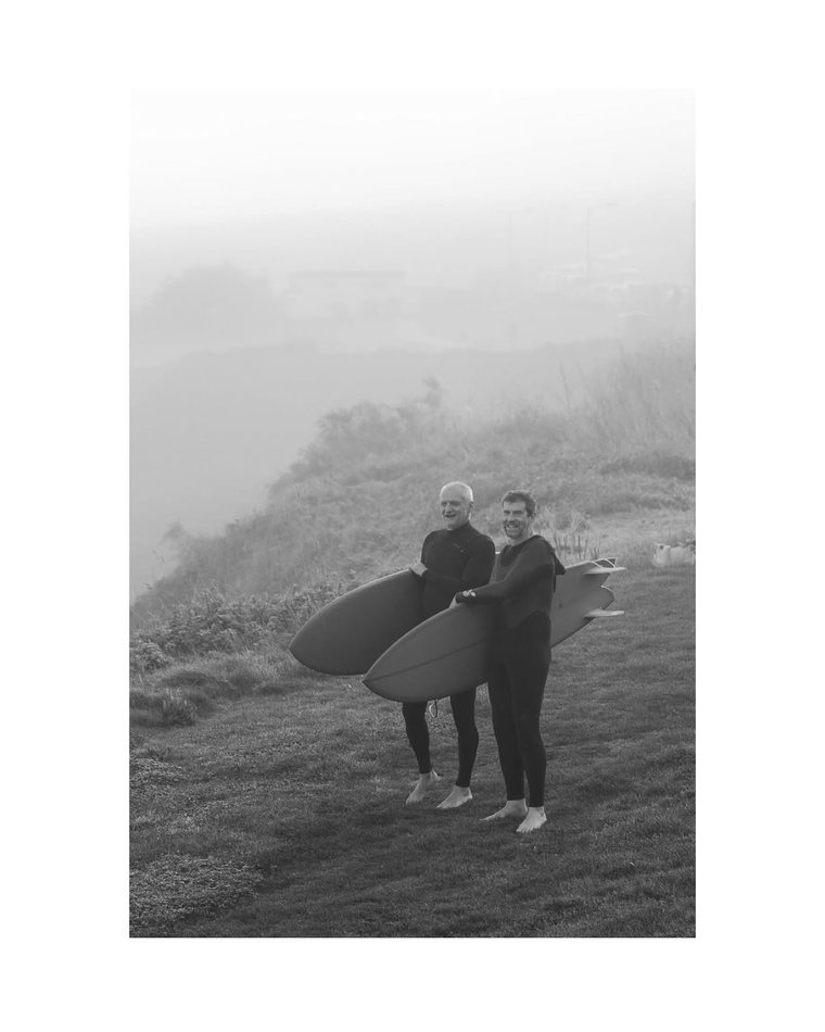 Two surfers carrying boards through the mist